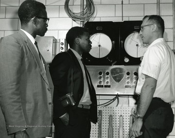 Three men (two African-American, other white) look at gauges on dairy equipment. 