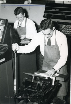 Two students working with a printing press. 