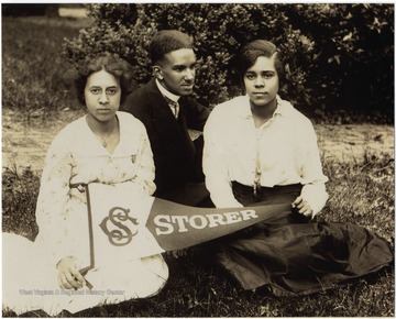 L to R:  Isabelle Stewart, Raymond McNeal and Odetta Johnson display a Storer pennant sitting on the campus lawn. All three students are listed as Honor Students in 1916.