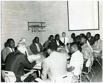Students of Agriculture from Tanganyika (now Tanzania) gathered around a table with WVU Faculty John Harvey and others.