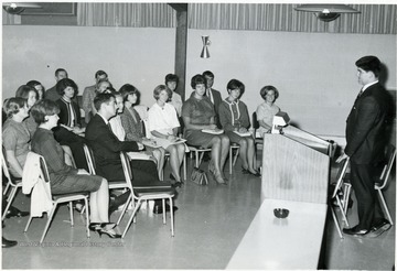 Russ Williams at a podium presenting to a roomful of attentive audience members. Some individuals' names are listed as follows: Jeri Degan, Sandy Buckley, Virginia Jackson and Rick Brown.