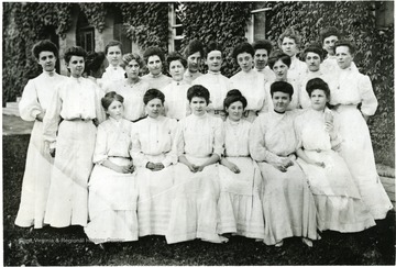 The picture shows a group of female students in front of a ivy covered building with a front arched entrance.