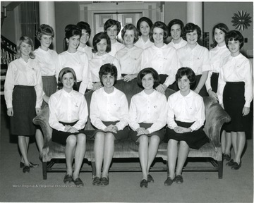 Group portrait of female members of WVU Panhellenic Council of 1966 in Elizabeth Moore Hall with their backs against the entrance; all the members dress alike in white top, dark bottom and in a pair of penny loafers.