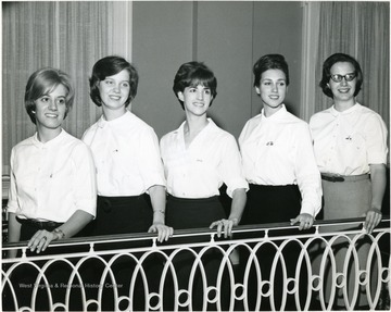 Executive Council of Associated Women Students pose for a photo op by lining up along the second floor railing of Elizabeth Moore Hall.  A uniform white is worn by all.
