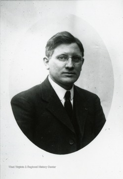 A bust portrait of an unidentified faculty in a suit and tie; he is clean shaven with cropped hair peppered with gray.  He is wearing wire rimmed glasses.  