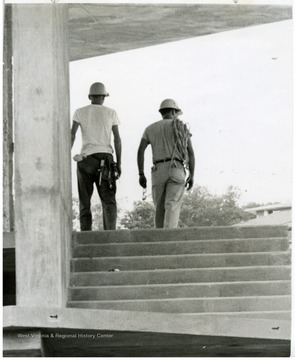 Two construction workers walking up the building's steps.