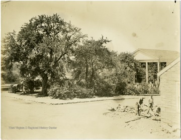 A view of Community Center in Arthurdale; two workers in the middle ground landscape in front of a house while other two workers in the foreground mix cement in front of the second structure. 