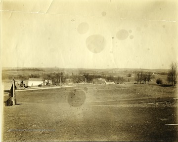 View of Arthurdale West Virginia; several houses, farm structures and vehicles are visible around an open field.