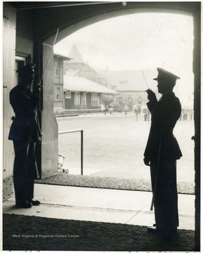 Two males in military uniform salute with saber held upward to the shoulder on an atrium of the building.  The caption on the original reads 'Cadet Col. Barnes. - Regimental Adjustment Ewing'.