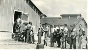 Shirtless R.O.T.C. cadets dressed in civilian clothes queue in line to enter a TC-47, Unit A structure.