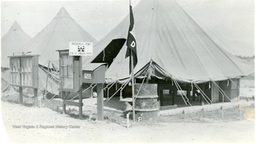 A view of R.O.T.C. Summer Training Camp; an entrance to the camp ground is shown, a few tents, a mail box, a flag on pole and bulletin boards stand by the entrance to the very first tent.