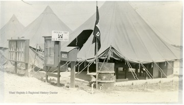 A view of ROTC Summer Training Camp; an entrance to the camp ground is shown, a few tents, a mail box, a flag on pole and bulletin boards stand by the entrance to the very first tent.  The sign reads 'Orderly Tent, CO D ENGRS ROTC'
