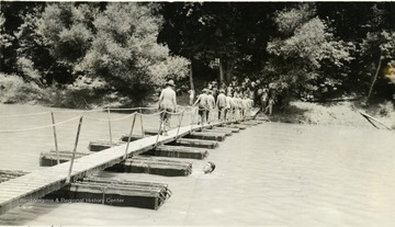 Cadets crossing a floating bridge; one cadet is in the water by a support.