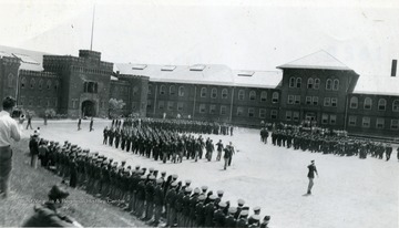 Cadets march in formation in Drill Field with Armory and Mechanical Hall in the background.