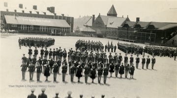 Cadets with sponsors in line facing officials on the Drill Field.  In the background are a building with 'McCartney' painted on a roof, Stewart Hall and Commencement Hall.