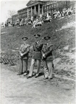 Three men of command standing in front of a campus building.