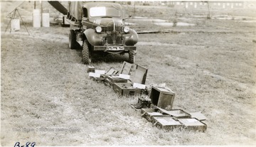 Boxes of military equipment and ammunition and a military truck are displayed on a camp ground.