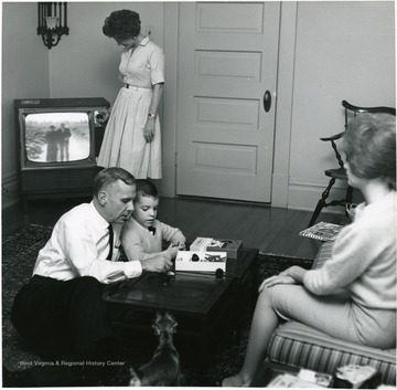 Children are Paula and Tommy. Family watches T.V. and plays a game.