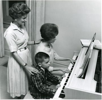 Children seated at piano with mom standing behind them, children's names are Paula and Tommy.