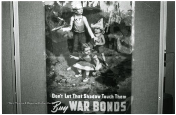 Exhibit in second floor gallery of Mountainlair. Poster says, 'Don't let that shadow touch them, buy war bonds.'