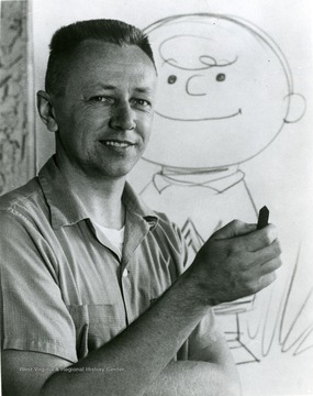 Creator of 'Peanuts' Schulz, Charles holds a block of pastel and stand in front of rough sketch of smiling Charlie Brown.