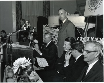 'Part of head table at Feb. 13, WVU Birthday Dinner.  From left to right: those identifiable include: Elvis Stahr, president of Indiana University and former WVU President; Dave Jacobs, executive secretary of WVU Alumni Association; Congressman Arch Moore; Mrs. Thomas White, Governor Hulett Smith; Thomas White, president of the Alumni Association; Dr. Harry B. Heflin, Acting WVU president; Jack Canfield, aide to Governor Smith; and Irvin Stewart, past president of WVU.'