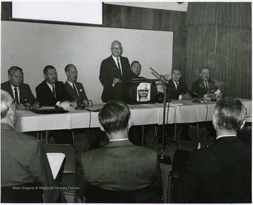 'Donovan H. Bond, Executive Director of the 100th Anniversary Observance, is seen speaking at the September 12, 1967 seminar, "The State University."  From left to right, others include: Keith Glancey, WVU Profesor of Education; Thomas Isaack, WVU Professor of Management; Thomas Canning, WVU Professor of Music; Ruel Foster, WVU Professor and Chairman of English and Chairman of the Seminar Planning Committee; Peter Muirhead, Associate U.S. Commissioner of Education; and James G. Harlow, President of WVU.'
