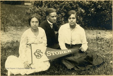 Isabelle Stewart, Raymond McNeal, and Odetta Johnson sit on the lawn at school holding a school pennant.