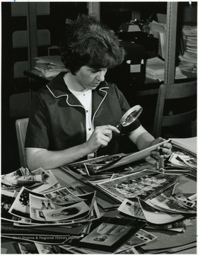 Blackwell, Judy, Secretary of the West Virginia Regional History Collection examines photos with a magnifier.