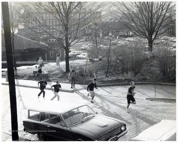 A scene from Greek Week events 'Hill Climb' showing members of Fraternity running up the North High Street.  In the background Administration Building, Old Buildings and Grounds and Security headquarters, Chemistry Building and Armory are also shown. 
