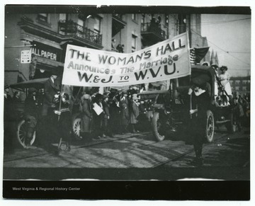 Female students of the Women's Hall march in parade on High Street holding banner announcing 'The Marriage W.& J. to WVU'.