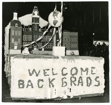 A float in homecoming parade depicting Woodburn Hall with a banner 'Welcome Back Grads'.