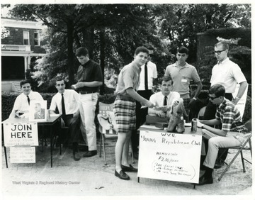 At the Young Democrats table, left to right, Rodney Pyles, Hugh Martin, and Wayne Brown (Standing.)  At the Young Republicans table, seated with white shirt, black tie, is Larry Dodd.  Standing directly behind Dodd, is Larry Crawford.