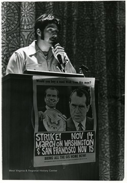 Richard Franzblau speaks in Mountainlair at a podium flanked with a poster with the image of President Richard Nixon, asking "Would you buy a used WAR from this man?  Strike Nov 14. March on Washington and San Francisco Nov 15.  Bring all the GIs home now."