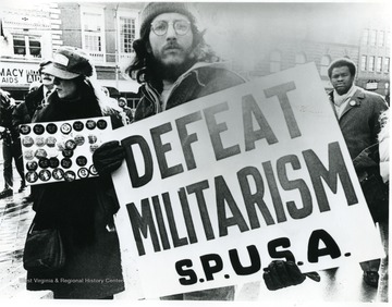 Students march from Mountainlair to Courthouse Square to protest against the military draft system.  Male student holds sign that reads, 'Defeat Militarism. S.P.U.S.A.'