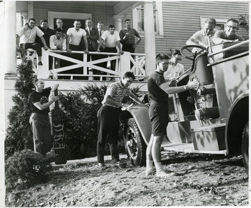 Potential members of the fraternity clean the truck and the members watch.