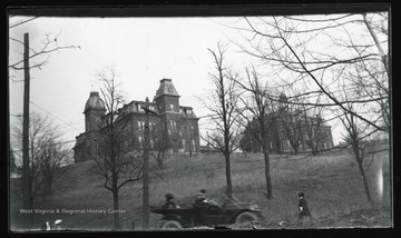 A view of Woodburn Hall (left) and Martin Hall (right) from Beechurst Avenue.  A motor car and a pedestrian are also in the shot.