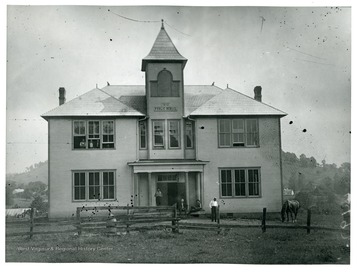 A view of school house that has a sign ' 1910, PUBLIC SCHOOL' on a bell tower. 
