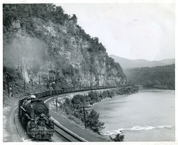 A View of the Norfolk and Western Railway between a river and a rock face. 