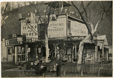 L. F. Randolph with dog and three women in front of store.  One woman is holding a guitar.