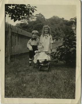 Three children of varying ages are playing in a yard surrounded by a picket fence. 