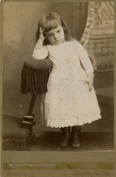 A cabinet card portrait of an unidentified little girl wearing a lace trimmed dress and high buttoned shoes and a look of boredom. Inscribed on the back of the photograph, "Merry Christmas and Happy New Years to Uncle 'Pug.'"