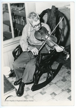 Older man in a rocking chair plays the fiddle.