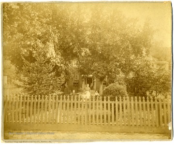 'First home of M. H. Dent and family--located on Front Street Grafton, W. Va., facing creek - at end of present South Side bridge.  Mrs. Dent, Carrie & Herbert in foreground - unidentified girl at corner of house.  Probably taken around 1885.'