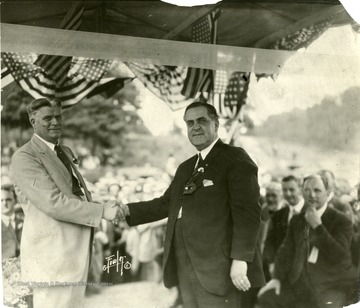 Governor Ephraim Morgan shaking hands with an unknown individual at an outdoor political gathering.