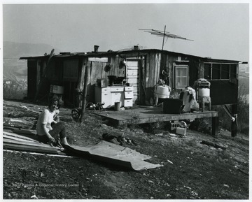 A woman sitting in the yard with a child outside a home.