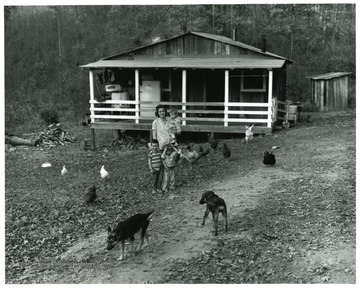 A woman with three children standing in their yard surrounded by dogs and chickens.