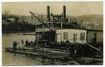 Postcard photograph of the steamboat 'Columbia' docking at the wharf on the Monongahela River at Morgantown next to a towboat and a ferry loaded with wagons, buggies and riders on horseback.