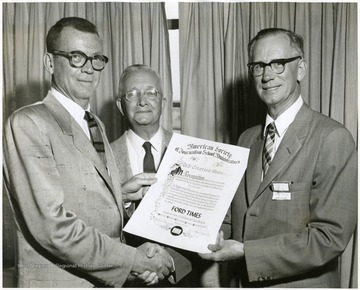 A photograph of a man being presented with a citation of merit.