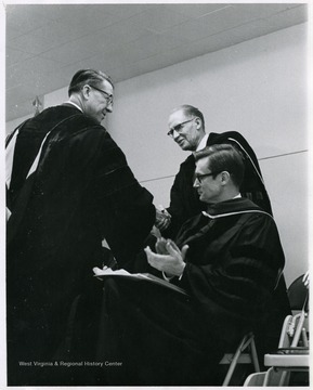 Harry Heflin (standing, left), acting president; Earl L. Core (standing, right), Professor of Biology; and Wesley Bagby (seated), Professor of History at a graduation ceremony.